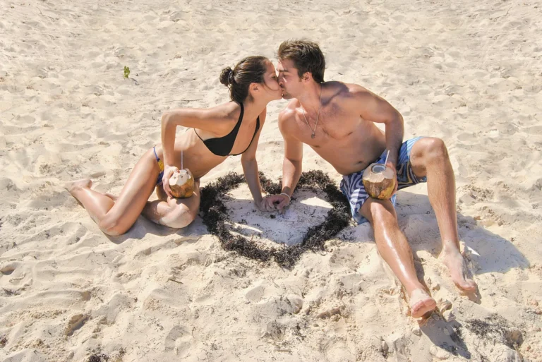 A couple on the beach beside a heart laid out in shells