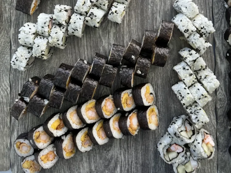 Sushi rolls laid out on wood, including maki, sesame California and shrimp tempura, served as premium cold bites on board