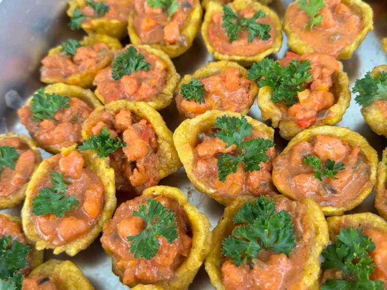 Plantain mofonguito cups filled with shrimp in creole sauce and topped with parsley, served as premium hot bites on board